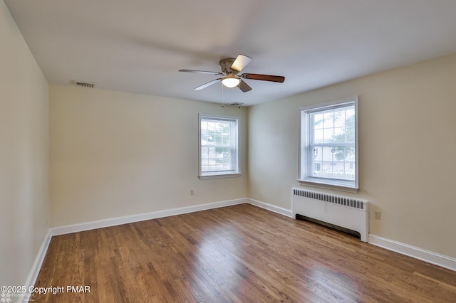 empty room with visible vents, a ceiling fan, wood finished floors, radiator, and baseboards