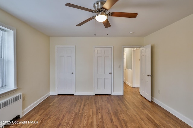 unfurnished bedroom with a ceiling fan, radiator heating unit, wood finished floors, and baseboards