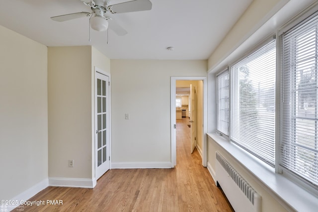 spare room featuring radiator, light wood-style floors, baseboards, and ceiling fan