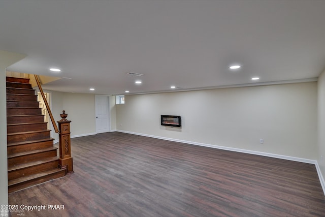 finished below grade area with baseboards, recessed lighting, stairs, dark wood-type flooring, and a glass covered fireplace
