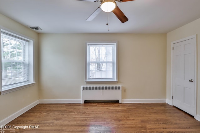 spare room featuring radiator heating unit, wood finished floors, visible vents, and a wealth of natural light
