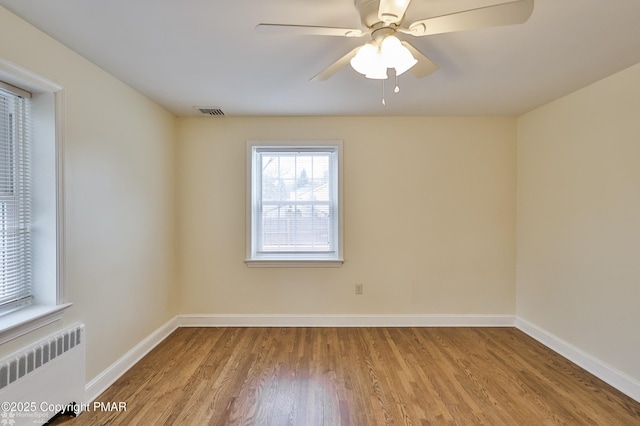empty room featuring visible vents, radiator, ceiling fan, baseboards, and wood finished floors