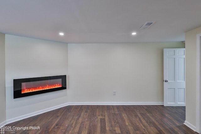 unfurnished living room with visible vents, dark wood-type flooring, baseboards, recessed lighting, and a glass covered fireplace