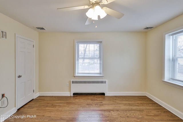 empty room with visible vents, radiator heating unit, baseboards, and wood finished floors