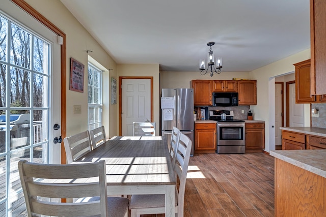 kitchen with wood finished floors, an inviting chandelier, light countertops, appliances with stainless steel finishes, and tasteful backsplash