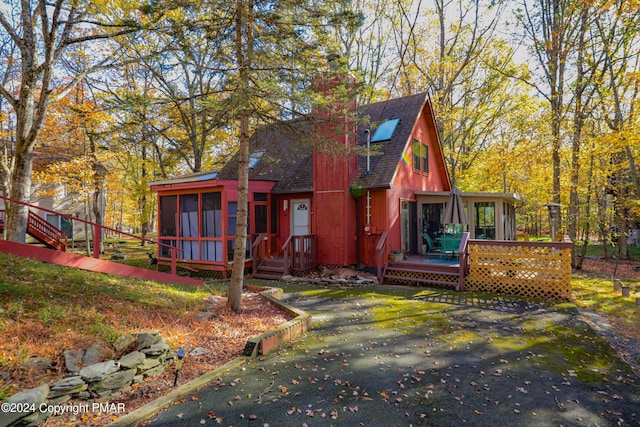 exterior space featuring a sunroom, a shingled roof, a chimney, and a wooden deck