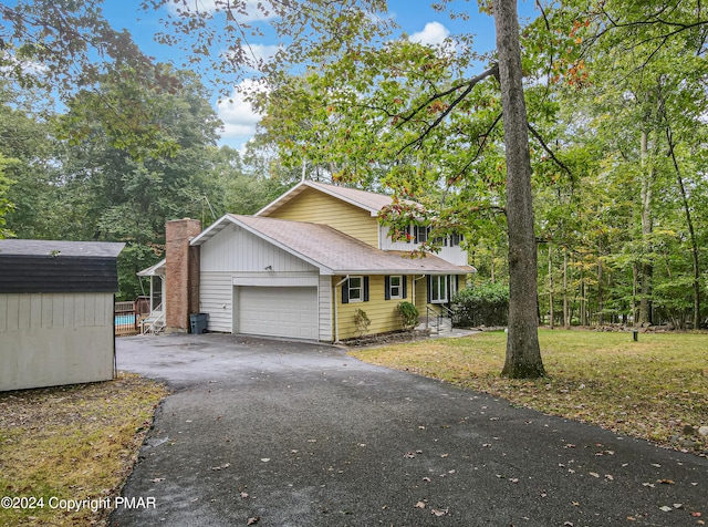 view of front of property with a shingled roof, aphalt driveway, an attached garage, a storage unit, and a front yard