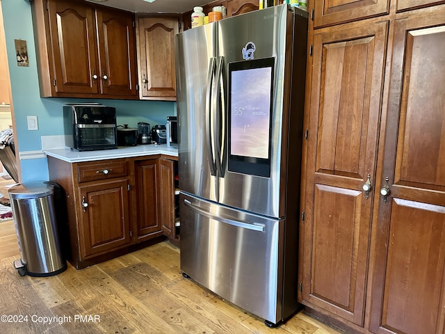 kitchen with light wood-type flooring, brown cabinetry, refrigerator with glass door, and light countertops