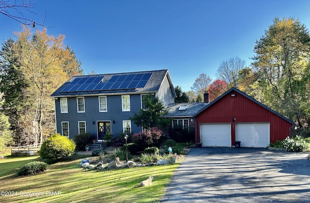 colonial home with driveway, a chimney, an attached garage, roof mounted solar panels, and a front lawn