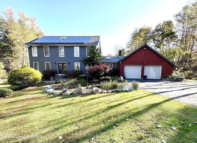 colonial home with roof mounted solar panels, aphalt driveway, and a front yard