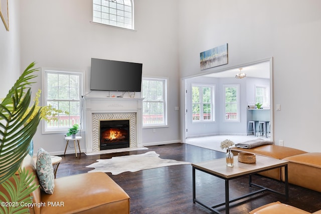 living room with a towering ceiling, baseboards, wood finished floors, and a glass covered fireplace