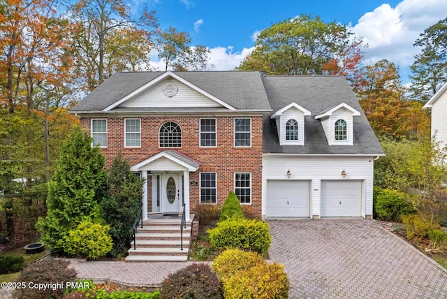 view of front of property featuring roof with shingles, brick siding, decorative driveway, and an attached garage