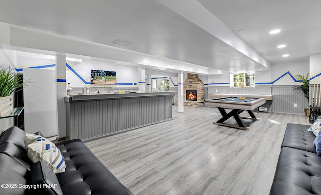 rec room with a wainscoted wall, recessed lighting, a stone fireplace, wood finished floors, and billiards