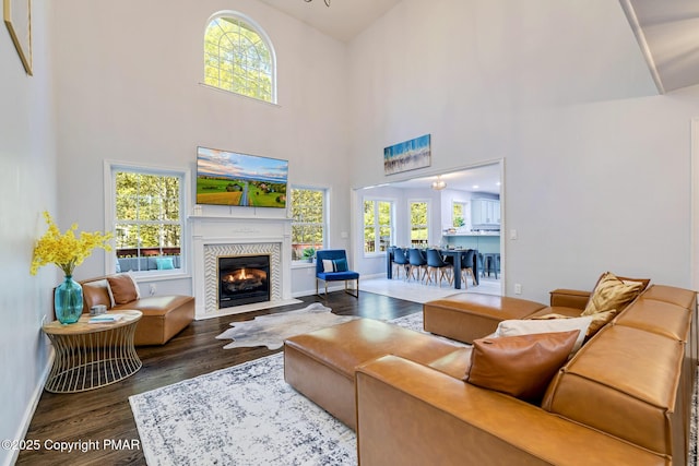 living room with a fireplace with flush hearth, wood finished floors, a towering ceiling, and baseboards