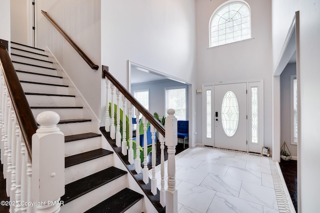 entryway with marble finish floor, stairway, and a towering ceiling