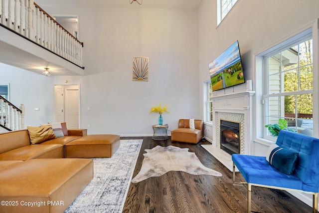 living area featuring a fireplace, wood finished floors, a towering ceiling, baseboards, and stairs