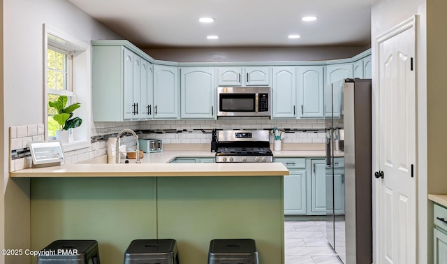 kitchen featuring decorative backsplash, appliances with stainless steel finishes, a peninsula, marble finish floor, and recessed lighting