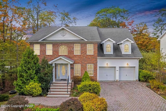 view of front of home with decorative driveway, brick siding, and an attached garage