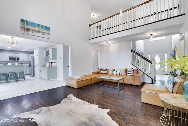 living area featuring light wood-style flooring, a high ceiling, stairway, and baseboards