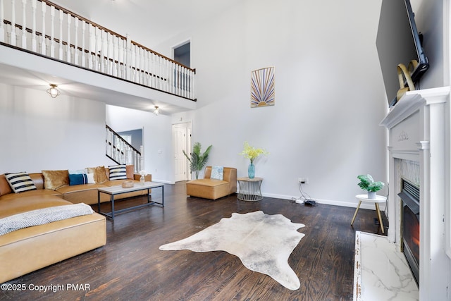 living area with wood finished floors, a towering ceiling, a high end fireplace, stairs, and baseboards