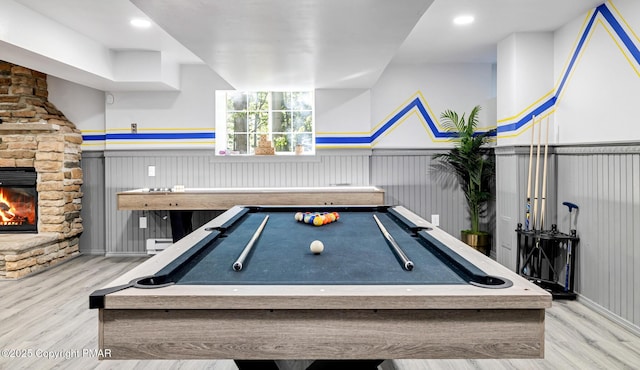 recreation room featuring a stone fireplace, billiards, light wood-type flooring, and baseboard heating