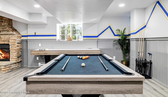 game room with a baseboard heating unit, a wainscoted wall, a stone fireplace, and wood finished floors