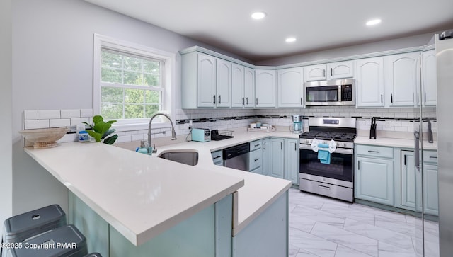 kitchen featuring a peninsula, a sink, marble finish floor, appliances with stainless steel finishes, and backsplash
