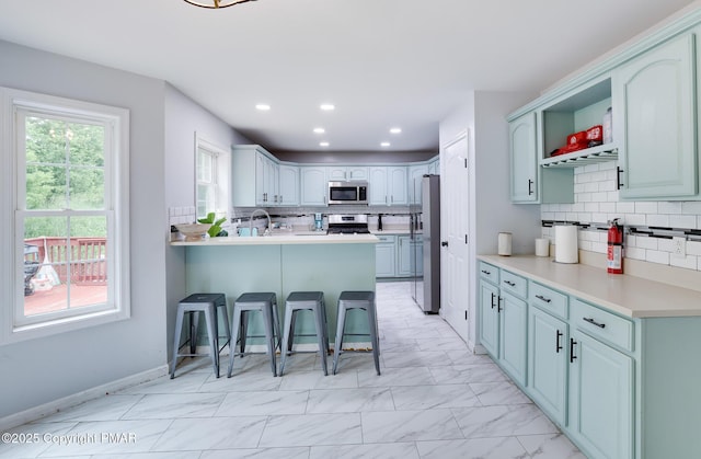 kitchen with stainless steel appliances, a breakfast bar, a peninsula, marble finish floor, and light countertops