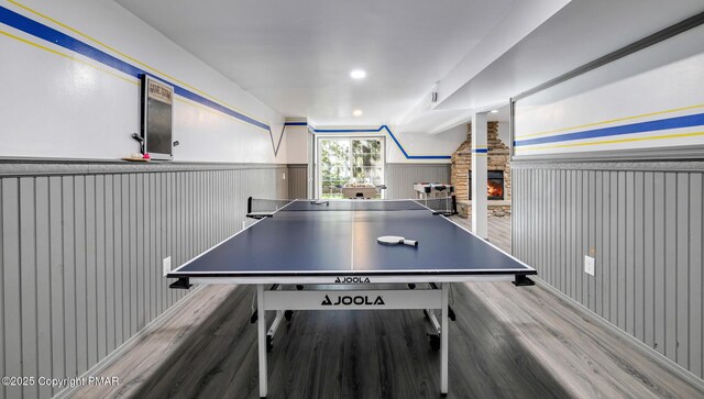 recreation room with recessed lighting, a wainscoted wall, a stone fireplace, and wood finished floors