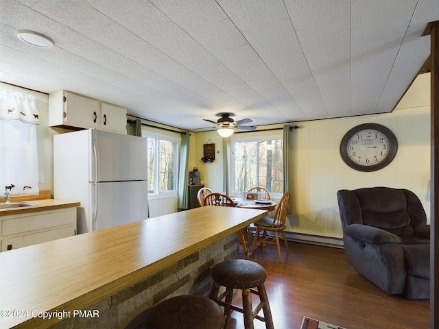 kitchen with dark wood-type flooring, sink, white refrigerator, baseboard heating, and cream cabinets