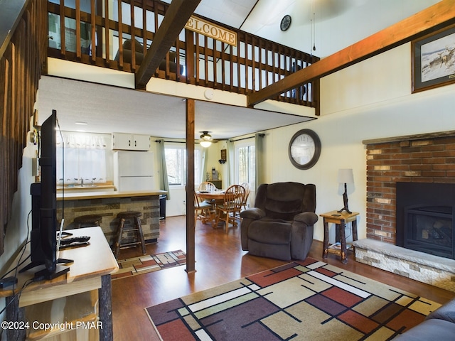 living room with ceiling fan, dark hardwood / wood-style floors, a brick fireplace, and a towering ceiling