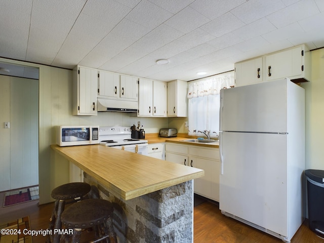 kitchen featuring sink, white appliances, a kitchen bar, dark hardwood / wood-style flooring, and kitchen peninsula