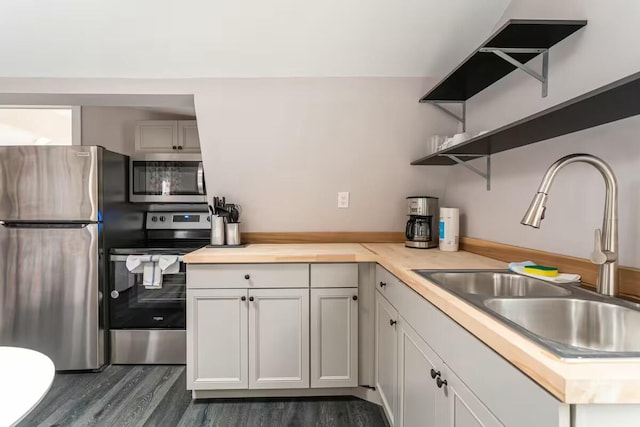 kitchen featuring open shelves, dark wood-style flooring, a sink, stainless steel appliances, and light countertops