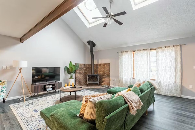 living room with a skylight, a wood stove, ceiling fan, and wood finished floors