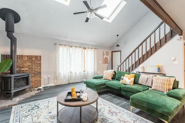 living room featuring ceiling fan, stairs, a skylight, a wood stove, and wood finished floors