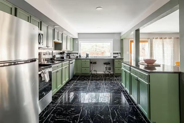 kitchen with green cabinetry, stainless steel appliances, dark countertops, and marble finish floor