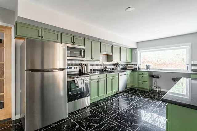 kitchen with marble finish floor, a sink, backsplash, stainless steel appliances, and green cabinetry