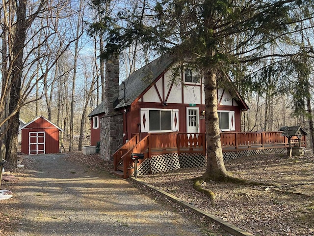 view of front facade featuring a storage unit, an outbuilding, a deck, roof with shingles, and a chimney