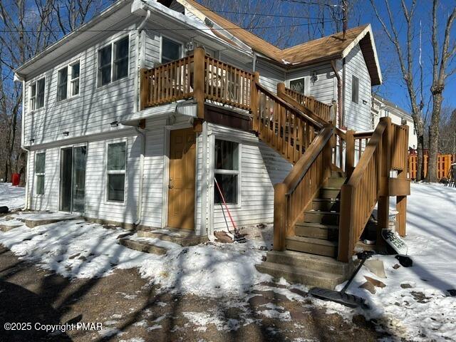 snow covered rear of property featuring stairway and a wooden deck