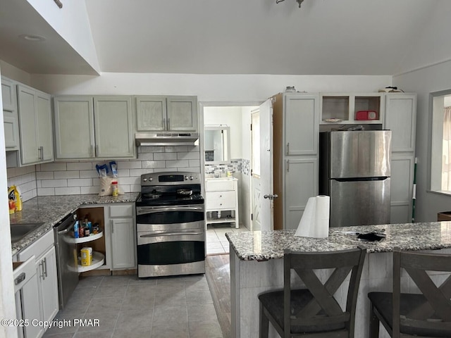 kitchen with appliances with stainless steel finishes, a breakfast bar area, light stone counters, and decorative backsplash