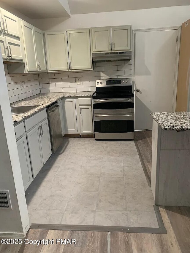 kitchen with stainless steel appliances, light wood-type flooring, backsplash, and light stone counters