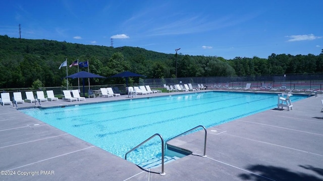 community pool featuring fence, a view of trees, and a patio area