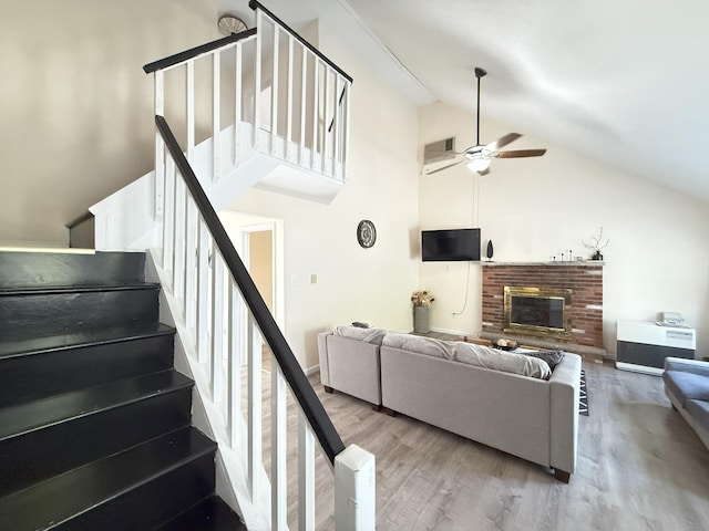 living area with wood finished floors, ceiling fan, high vaulted ceiling, stairway, and a brick fireplace