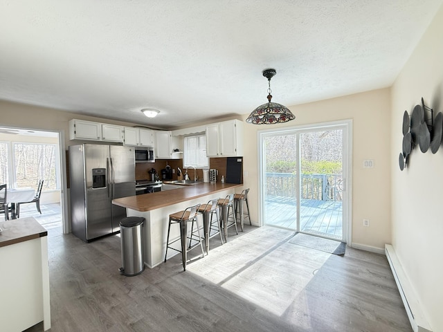 kitchen with appliances with stainless steel finishes, a baseboard heating unit, wood finished floors, a peninsula, and a textured ceiling
