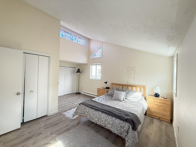 bedroom featuring a baseboard radiator, high vaulted ceiling, wood finished floors, a textured ceiling, and baseboards