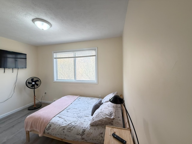 bedroom with wood finished floors, a textured ceiling, and baseboards