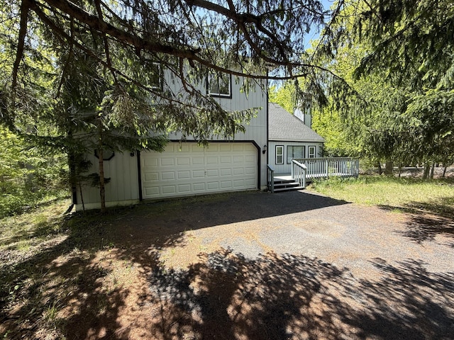 rear view of house featuring driveway, a deck, a garage, and a shingled roof