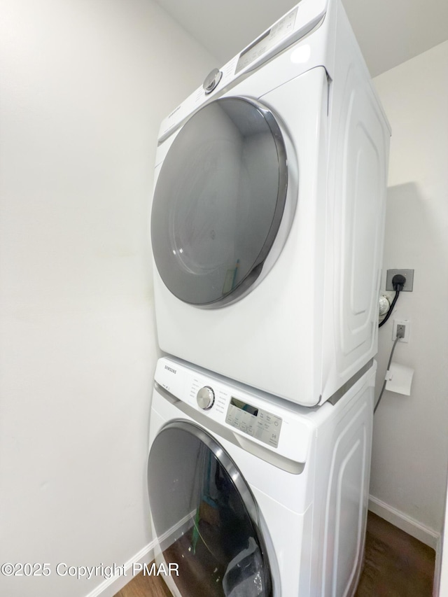 clothes washing area featuring laundry area, baseboards, stacked washer / dryer, and wood finished floors