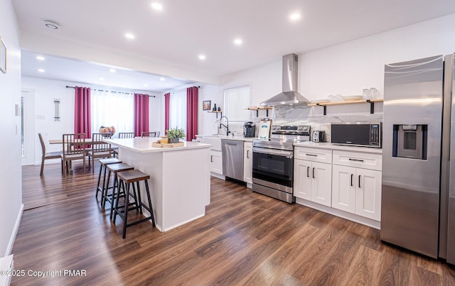 kitchen featuring stainless steel appliances, a breakfast bar, a kitchen island, wall chimney exhaust hood, and dark wood finished floors