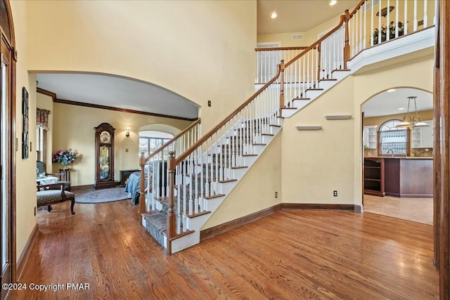 stairway featuring a towering ceiling, baseboards, arched walkways, and wood finished floors